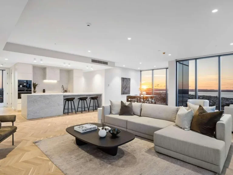 Fotografía profesional de arquitectura interior que muestra una sala y cocina de diseño contemporáneo, con grandes ventanales y vista panorámica al atardecer.